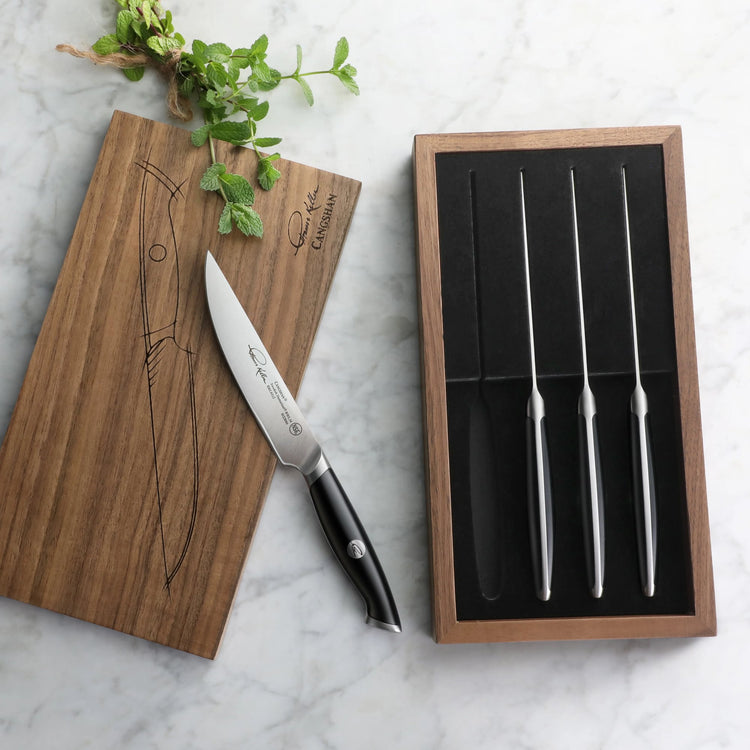 Four 5-inch steak knives with black handles in a walnut storage box, one knife outside on a wooden lid.