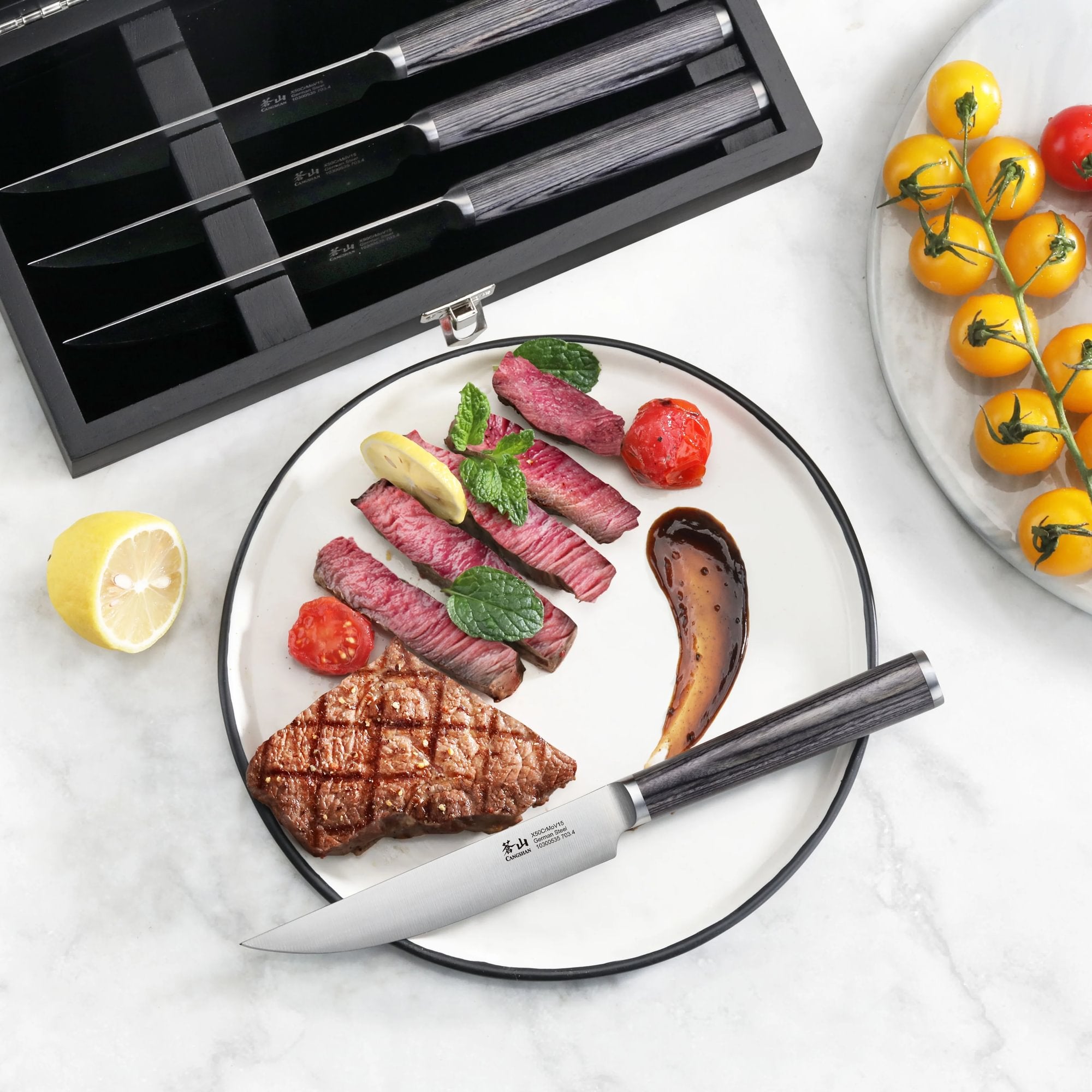 Four steak knives with pakkawood handles in a wooden box, one knife cutting sliced steak on a plate with grilled vegetables.