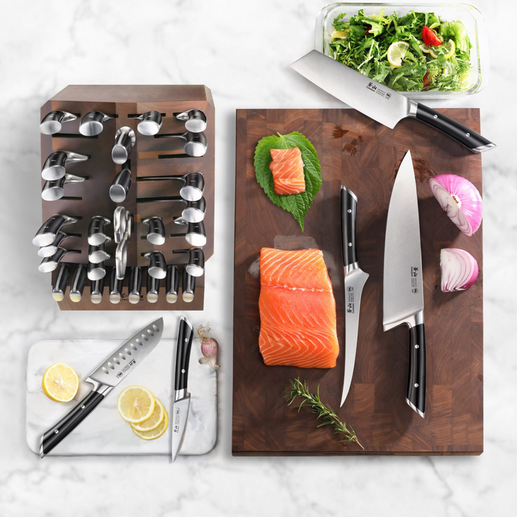 36-piece black-handled knife set in wooden block, with salmon, onion, lemon slices, herbs, and salad on cutting boards.