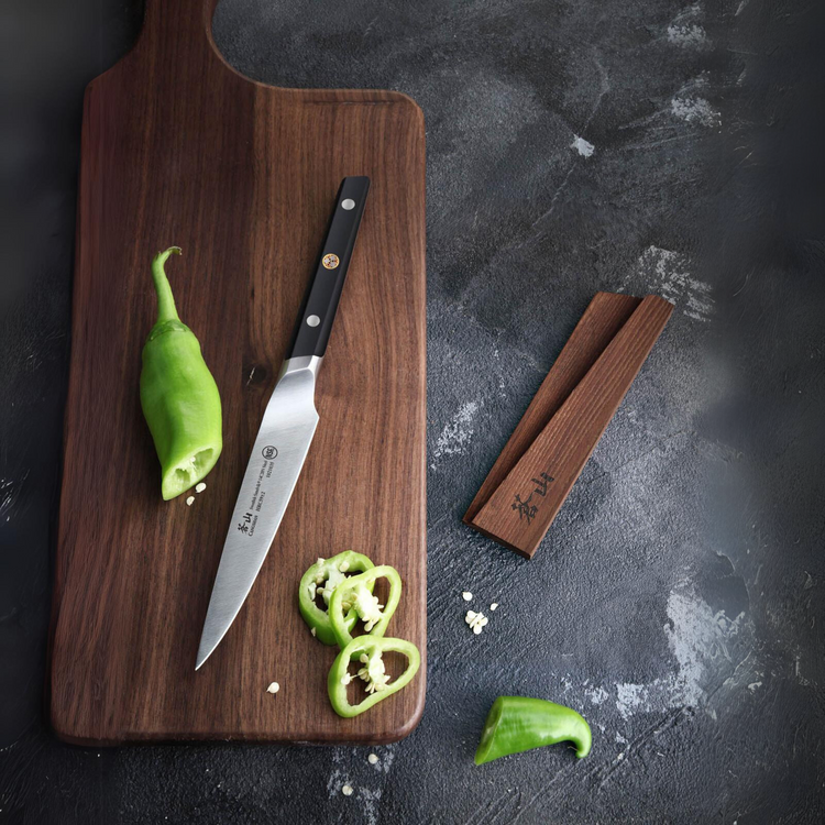 Wooden cutting board with a kitchen knife and sliced green chili peppers on a dark surface.