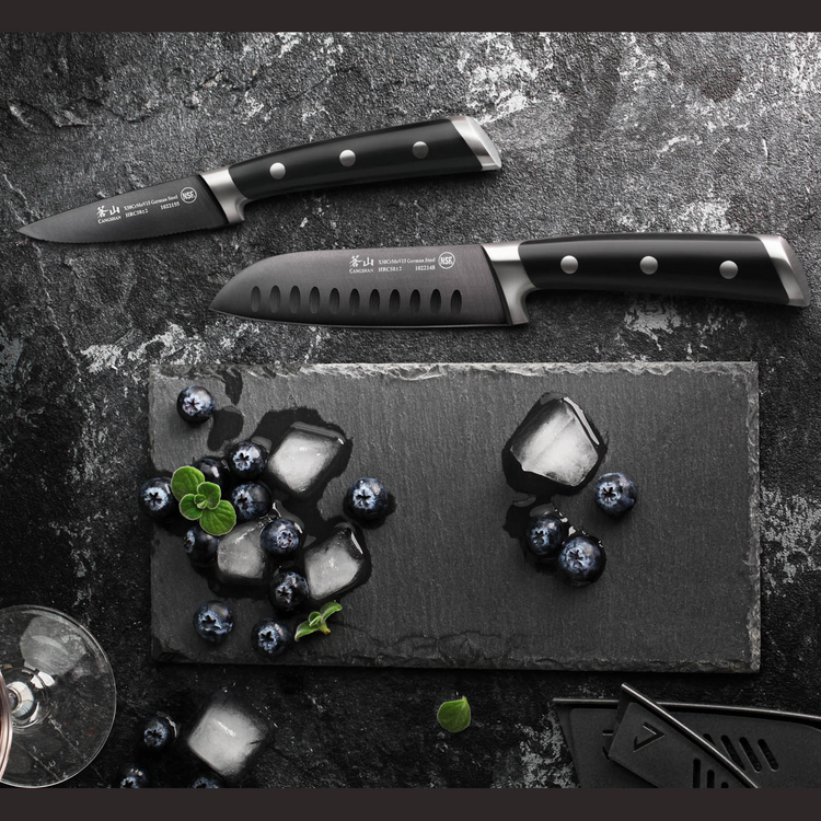 Two black-handled kitchen knives placed on a dark surface near blueberries and melting ice cubes on a slate board.