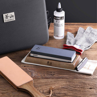 
                    
                      Dual-sided whetstone on wooden base with sharpening oil, cut-resistant glove, leather strop, and carrying case on wooden surf
                    
                  