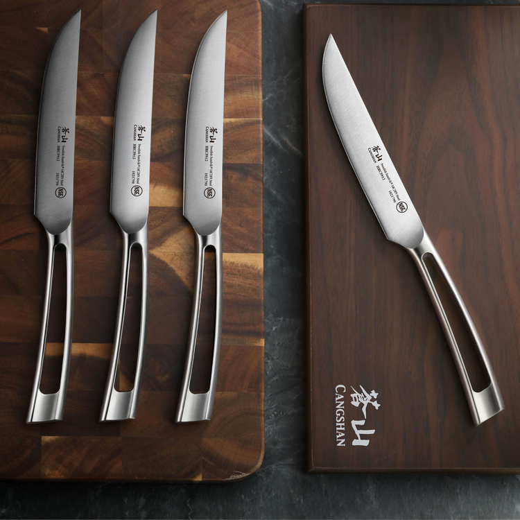 Four stainless steel steak knives with hollow handles displayed on two wooden boards, one branded with "CANGSHAN.
