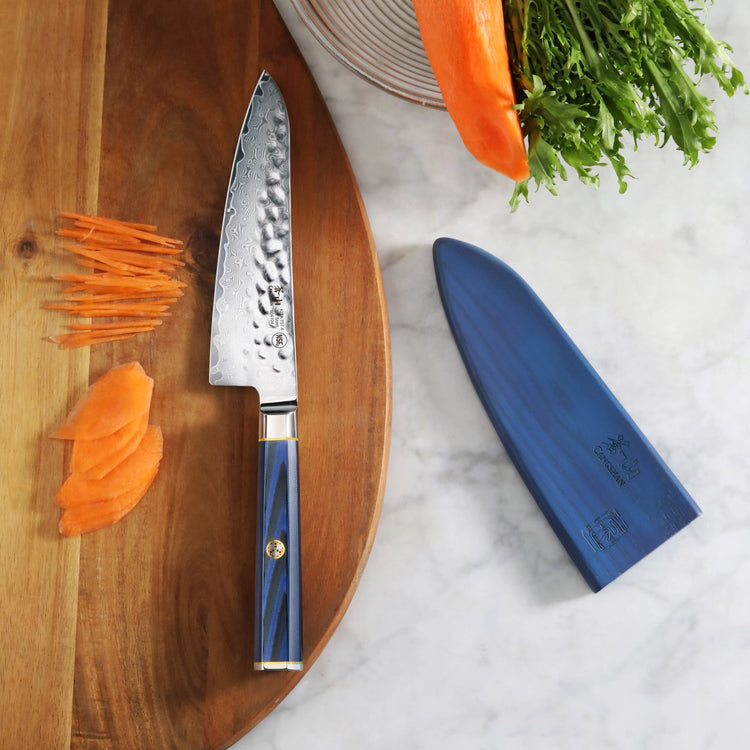 5.5-inch prep utility knife with blue handle and sheath, placed on a wooden board with sliced carrots nearby.