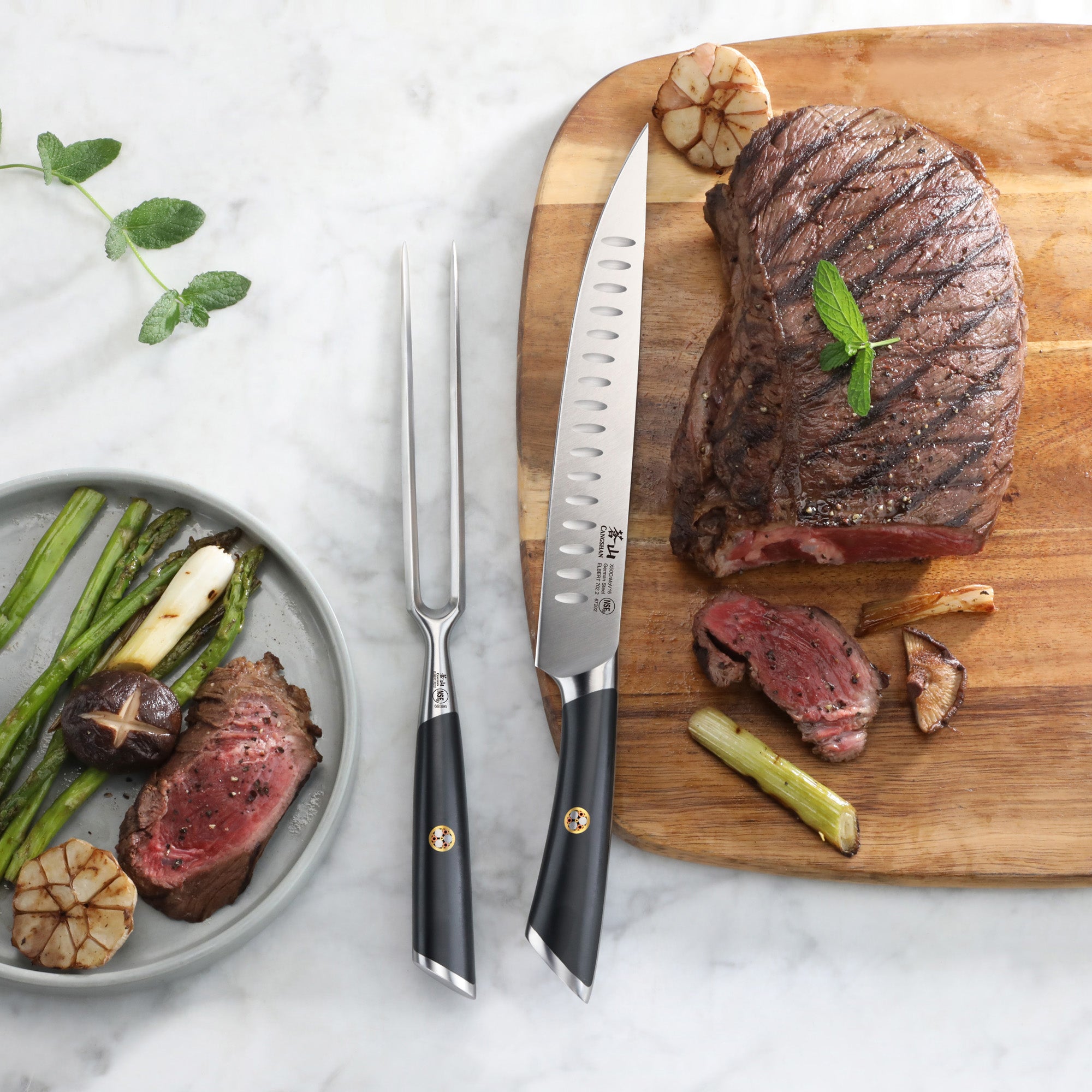 Two-piece carving set with a knife and fork beside a grilled steak on a wooden cutting board and a plate with sliced steak an