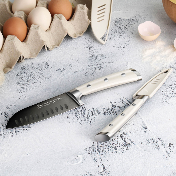 Two ceramic knives with white handles, one with a protective cover, next to a carton of eggs and cracked eggshells.