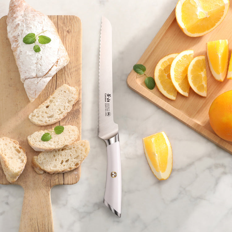 8-inch offset bread knife with serrated blade on marble surface between sliced bread and orange wedges on wooden boards.
