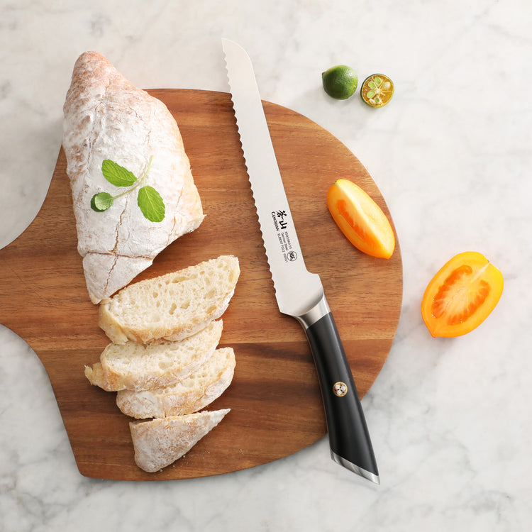 8-inch offset bread knife with black handle on wooden board next to sliced rustic bread and cut fruit pieces.