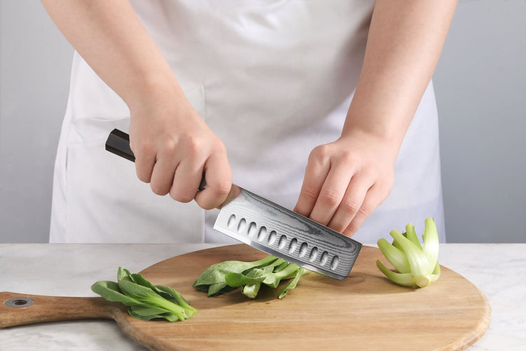 Chef using a MAYA Series 5-Inch Nakiri Knife X-7 Damascus Steel to chop green vegetables on a cutting board.