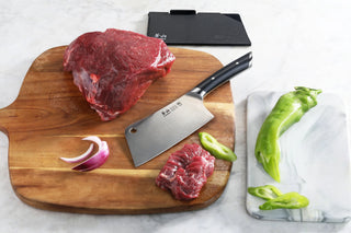 
                    
                      6-inch meat cleaver with black handle on wooden cutting board with raw beef, onion slice, and green peppers nearby.
                    
                  
