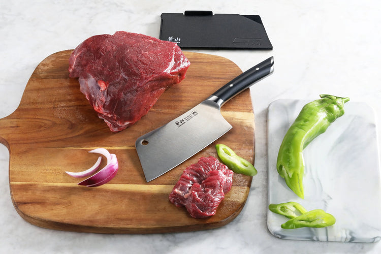 6-inch meat cleaver with black handle on wooden cutting board with raw beef, onion slice, and green peppers nearby.