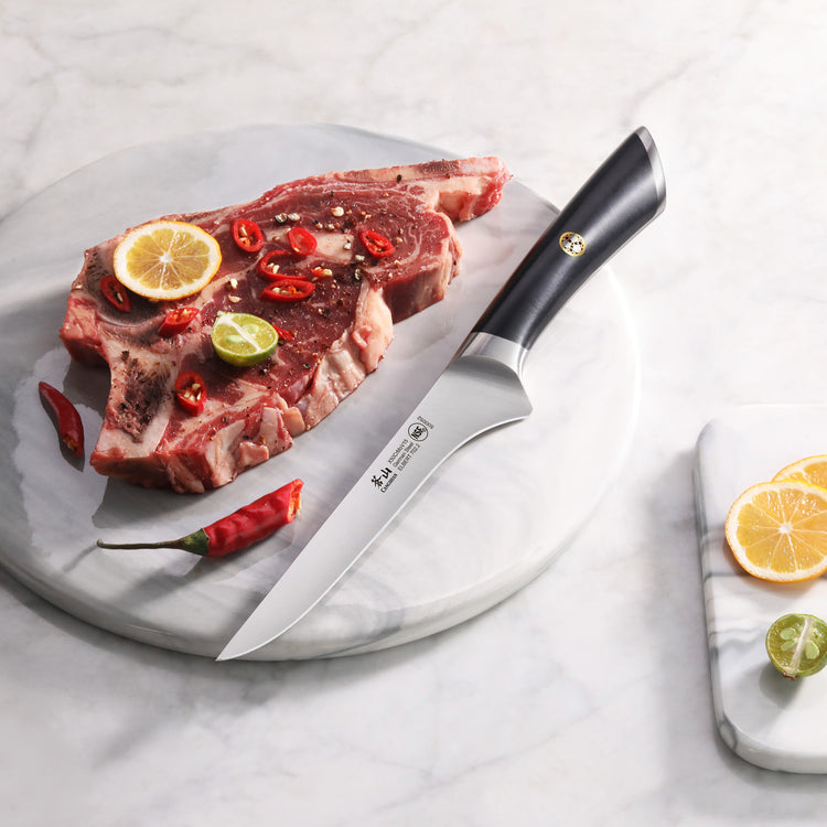 Boning knife with black handle on marble board next to raw steak garnished with chili, lemon, and lime slices.