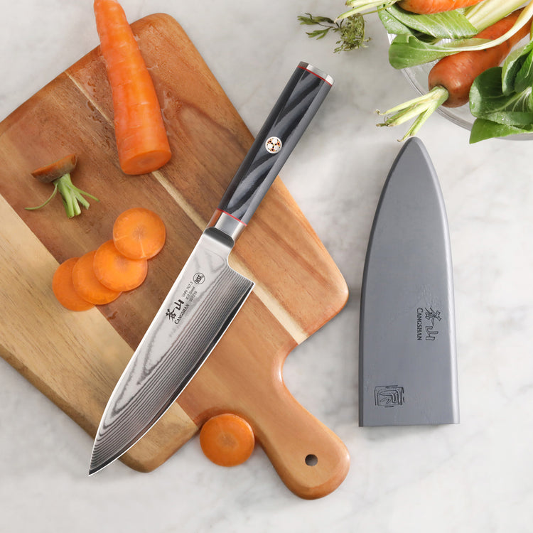 6-inch chef's knife with black handle and sheath on a cutting board with sliced carrots and greens nearby