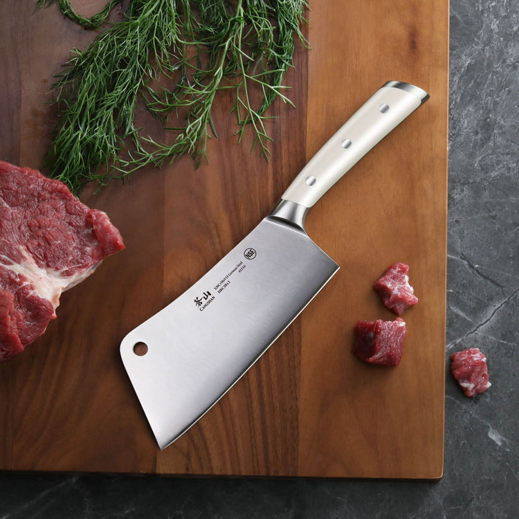 Cleaver knife with stainless steel handle on wooden cutting board next to raw beef and herbs.