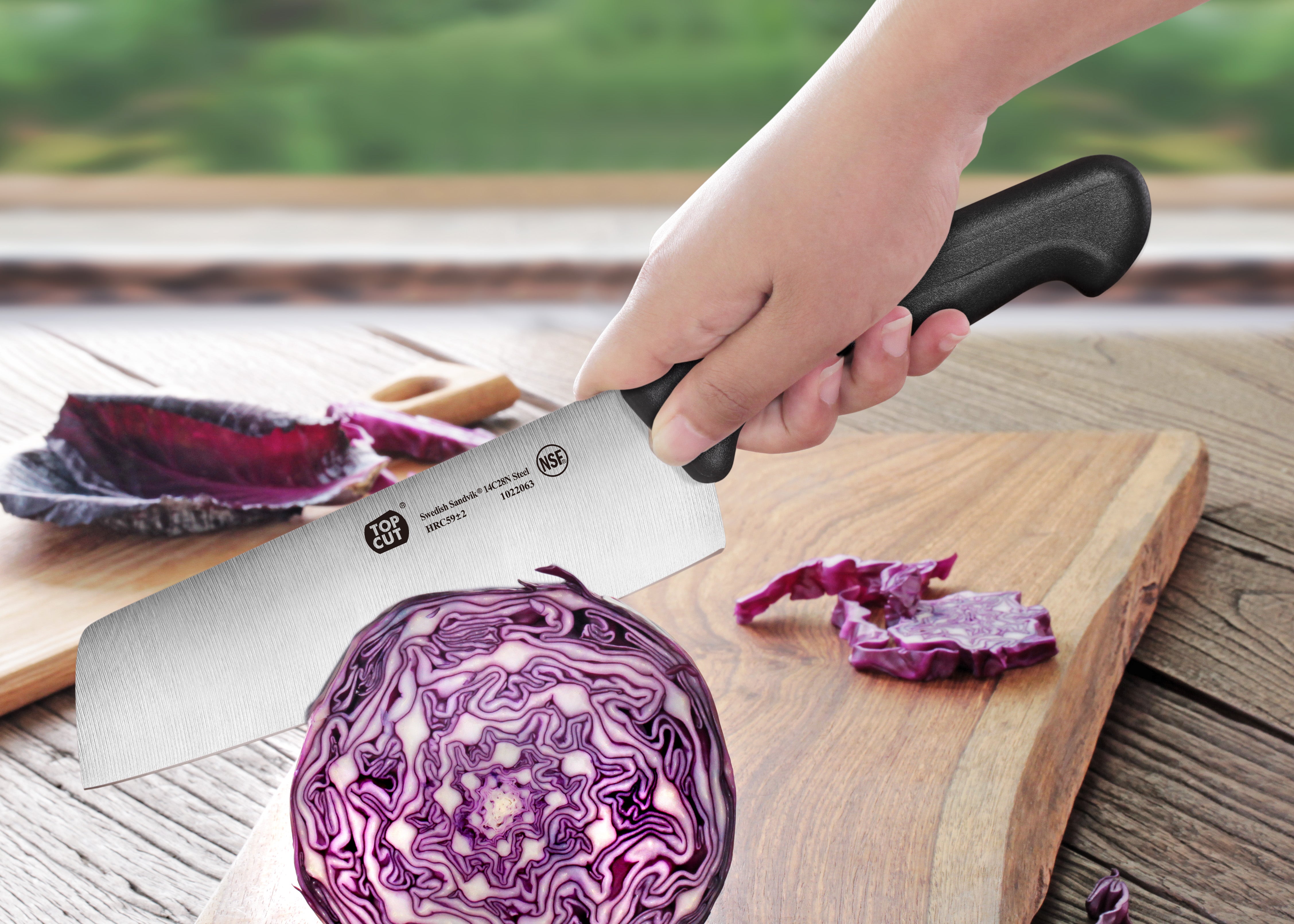 Hand holding a vegetable cleaver cutting a halved purple cabbage on a wooden cutting board.