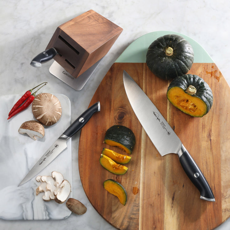 Four-piece knife set with black handles, wooden block, and sliced green squash on a wooden cutting board.