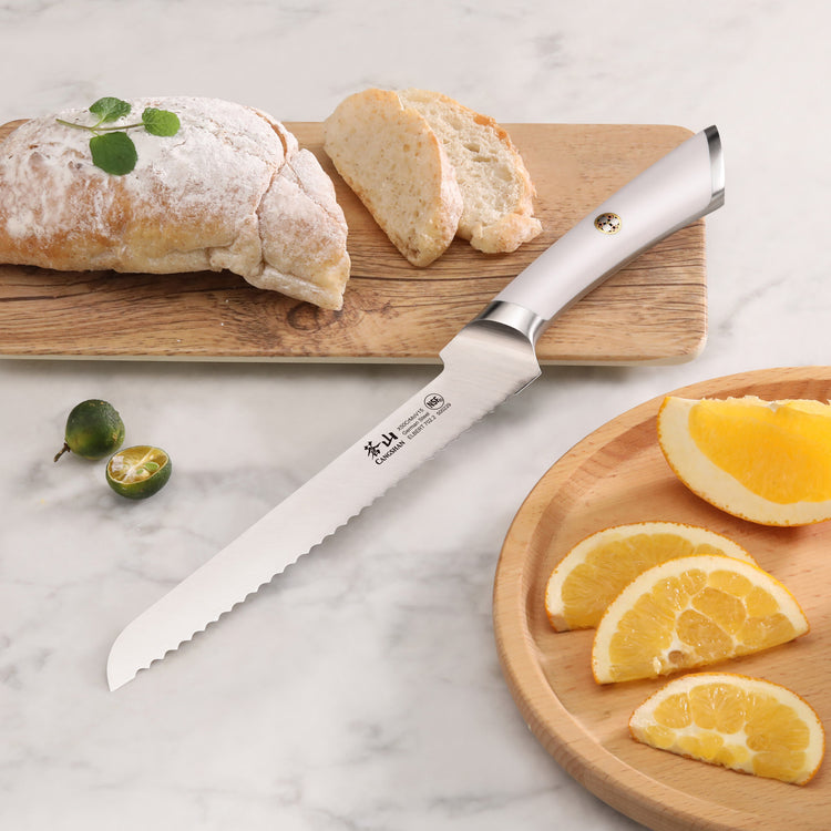 8-inch offset bread knife with serrated blade and white handle on marble surface, near sliced bread and orange wedges.