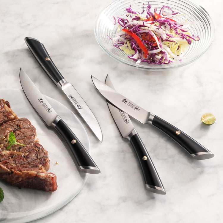 Four steak knives with black handles arranged on a marble surface near a cooked steak and a bowl of salad.