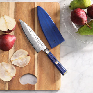 
                    
                      6-inch chef's knife with blue handle and sheath on wooden cutting board with sliced pears and whole pears nearby.
                    
                  
