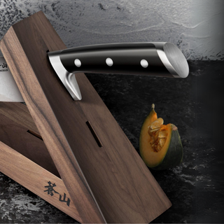 
                    
                      Walnut wood knife block holding a knife with a black handle, next to a cut piece of squash on a dark surface.
                    
                  