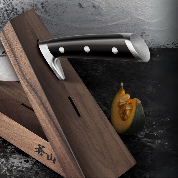 Walnut wood knife block holding a knife with a black handle, next to a cut piece of squash on a dark surface.