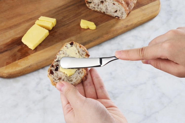Person spreading butter on a slice of bread using a small stainless steel butter knife.