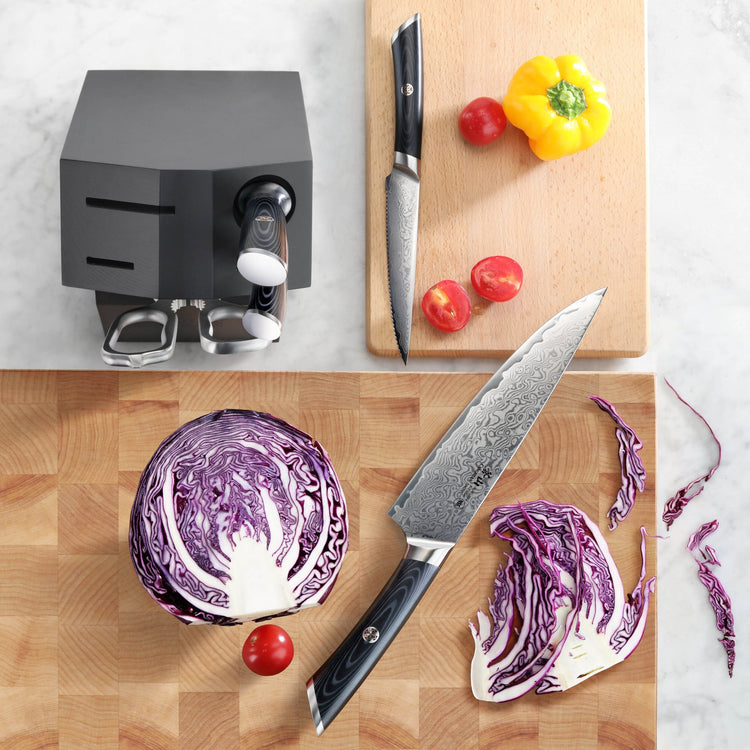 Six-piece knife set with two knives, a black knife block, and sliced red cabbage, cherry tomatoes, and a yellow bell pepper o