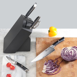 
                    
                      Black knife block with three knives inserted, one knife on a cutting board slicing purple cabbage, cherry tomatoes on a marbl
                    
                  