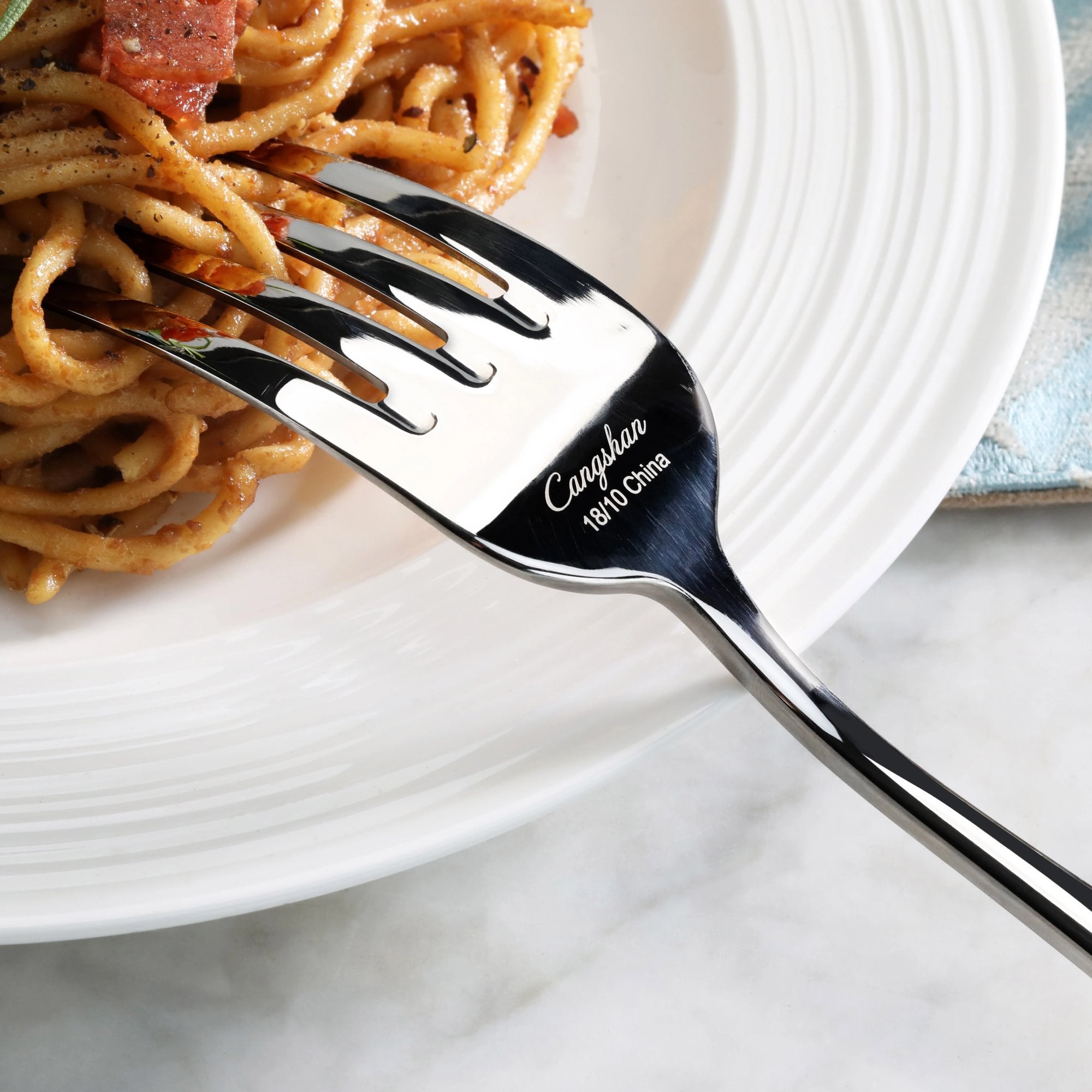 Serving fork with mirror finish holding spaghetti on a white ridged plate.