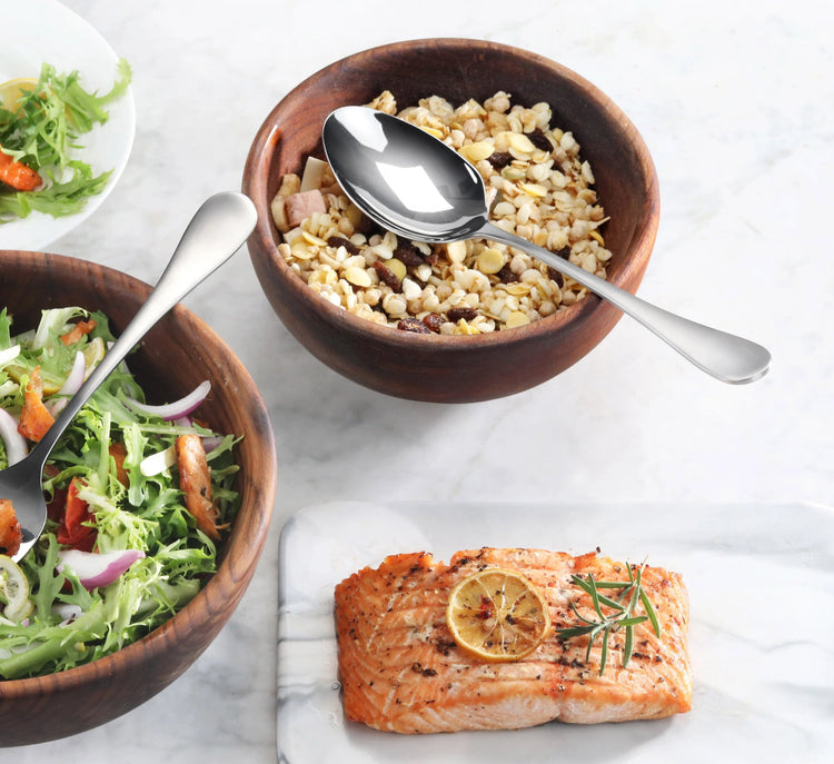 Serving spoon with matte finish handle resting on a wooden bowl filled with grains, next to a salad and cooked salmon.
