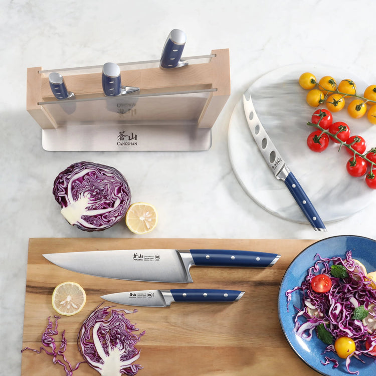 Seven-piece knife set with blue handles displayed with sliced cabbage, lemon, and cherry tomatoes on wooden and marble surfac