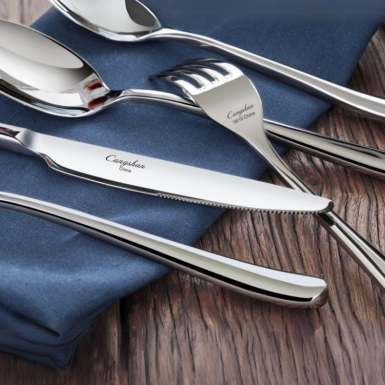 Set of polished stainless steel flatware including a knife, fork, spoon, and teaspoon on a blue napkin and wooden surface.