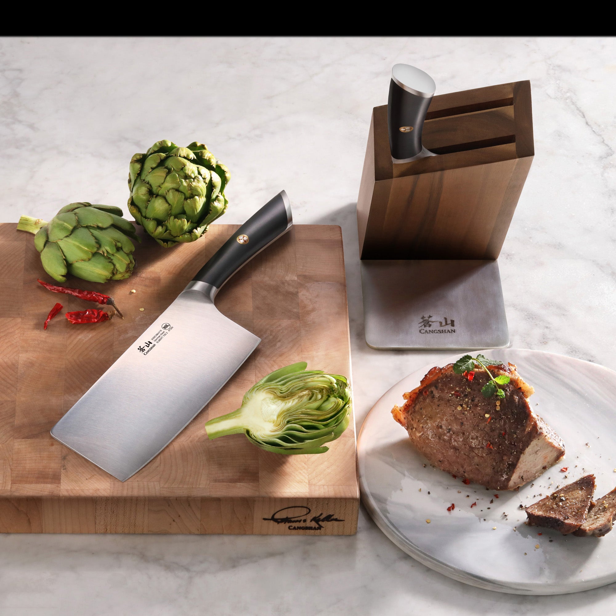 Cleaver knife on wooden cutting board with artichokes, knife block, and sliced cooked meat on plate.