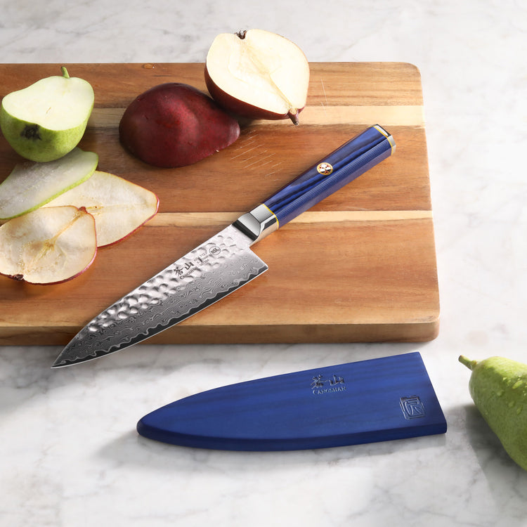 6-inch chef's knife with hammered blade and blue handle on wooden cutting board with sliced pears and blue sheath nearby.