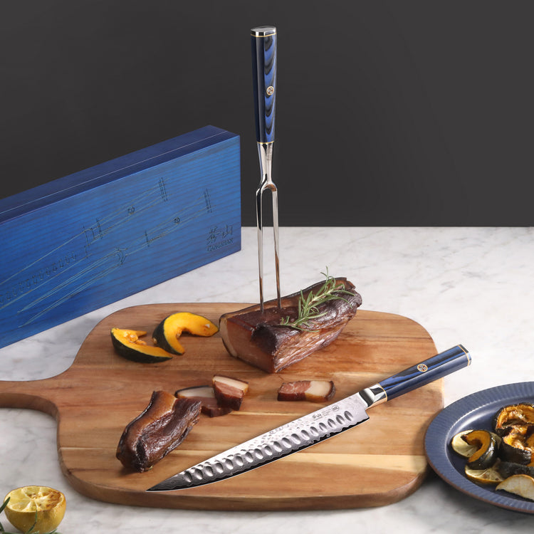 Two-piece carving set with blue handles, including a carving fork and knife, displayed with sliced meat and vegetables on a w