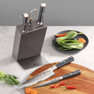 
                    
                      Knife block set with three knives and kitchen shears, placed on a countertop with vegetables and a wooden cutting board.
                    
                  