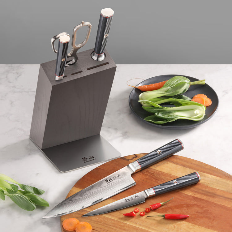 Knife block set with three knives and kitchen shears, placed on a countertop with vegetables and a wooden cutting board.