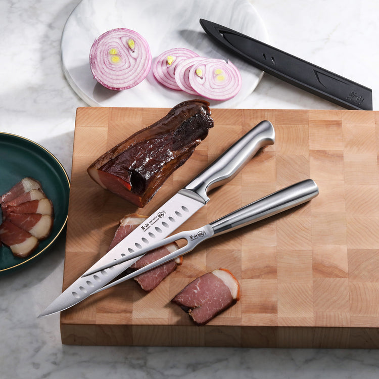 Two stainless steel carving knives on a wooden cutting board with sliced smoked meat and a plate of sliced red onion.