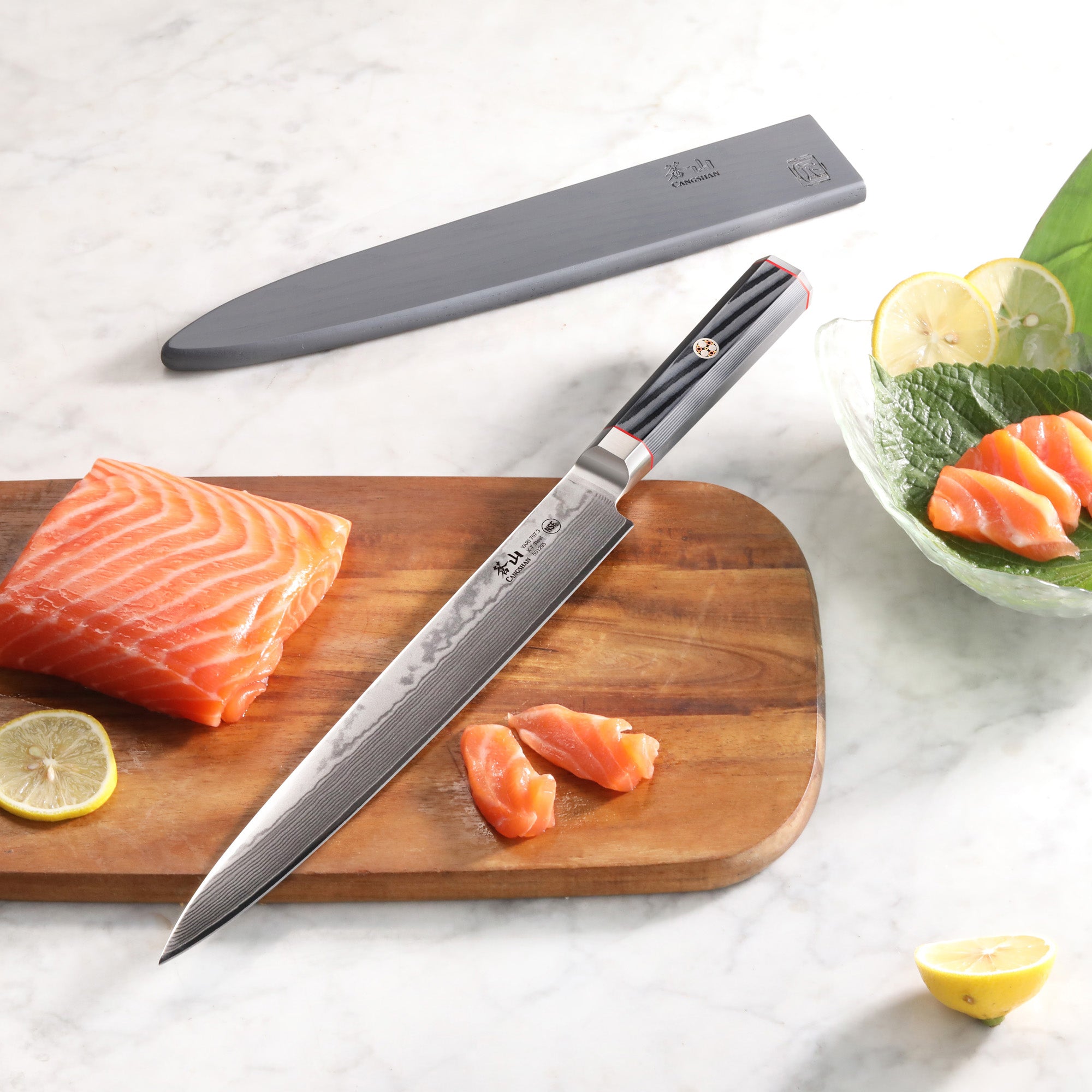 10-inch sashimi knife with patterned blade and black handle on wooden board next to sliced salmon and sheath.