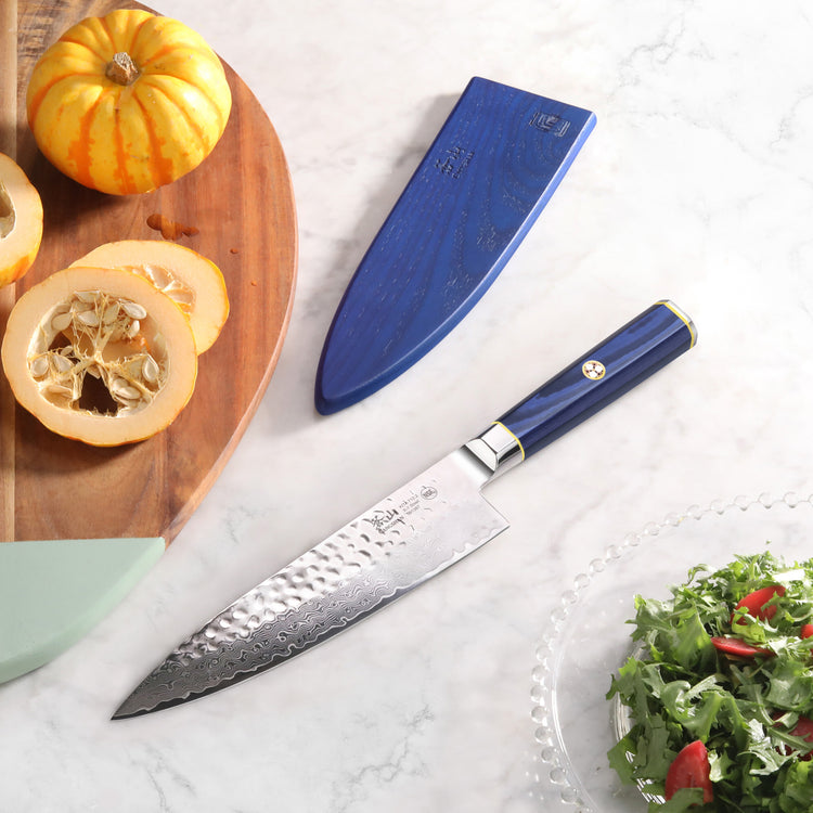 8-inch chef knife with blue handle and sheath, hammered blade pattern, next to sliced pumpkin and salad bowl.