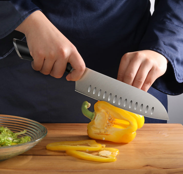 Person slicing a yellow bell pepper on a wooden cutting board with a 7-inch Santoku knife.