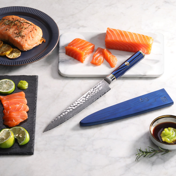 8-inch sashimi knife with blue handle and sheath next to sliced salmon, lime, soy sauce, and cooked fish on marble surface.