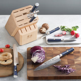 
                    
                      Wooden knife block with empty slots and three blue-handled knives, one slicing purple cabbage on a cutting board.
                    
                  