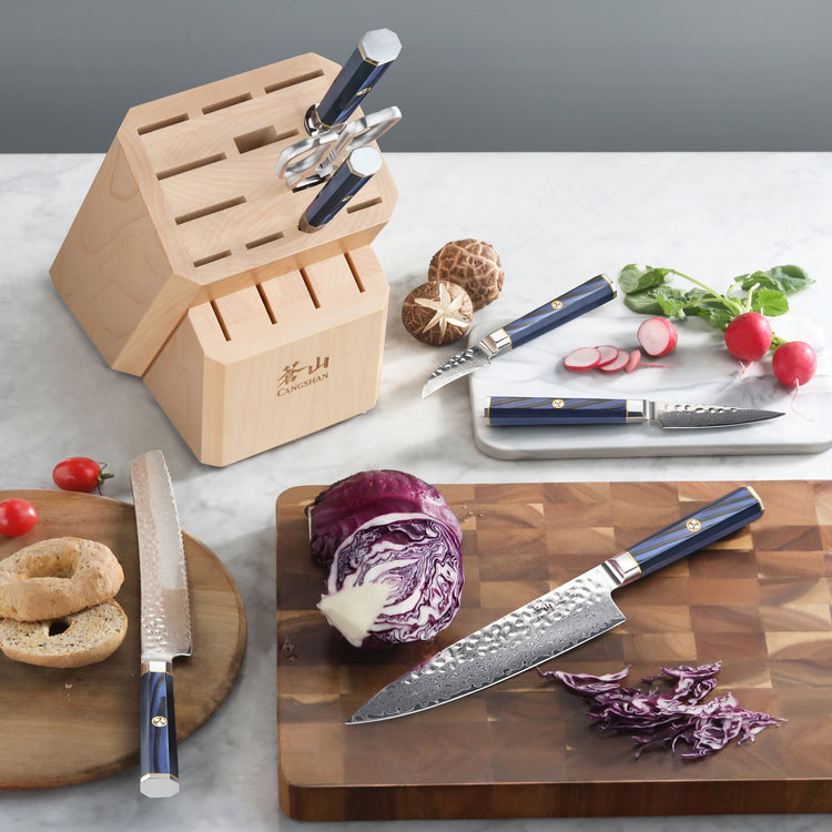 Wooden knife block with empty slots and three blue-handled knives, one slicing purple cabbage on a cutting board.