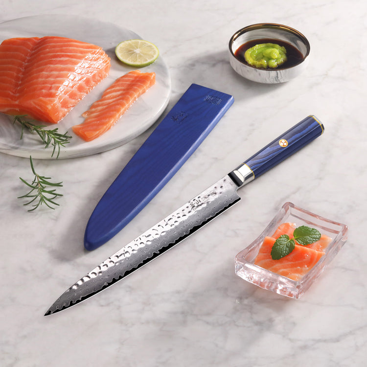 10-inch sashimi knife with blue sheath, hammered blade, next to sliced salmon, soy sauce with wasabi, and garnished sashimi.