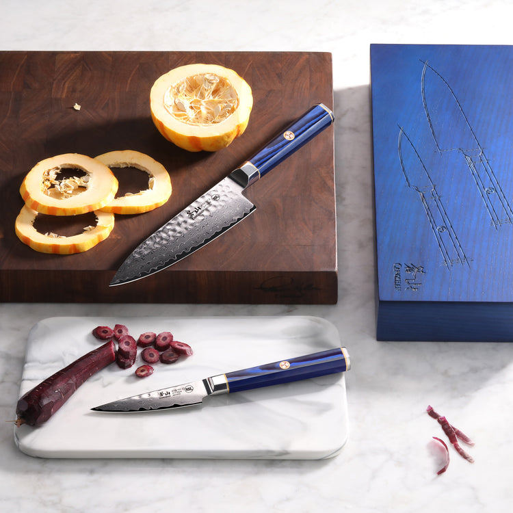Two blue-handled knives on cutting boards with sliced squash and octopus, next to a blue knife box with blade sketches.