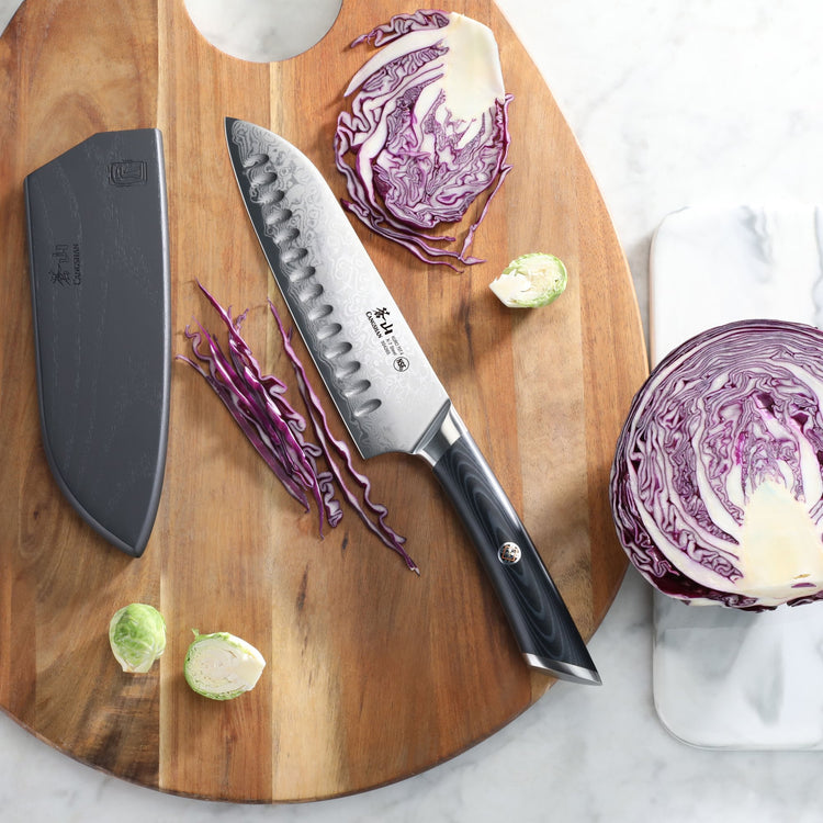 7-inch Santoku knife with black handle and sheath on wooden board, sliced red cabbage and Brussels sprouts nearby