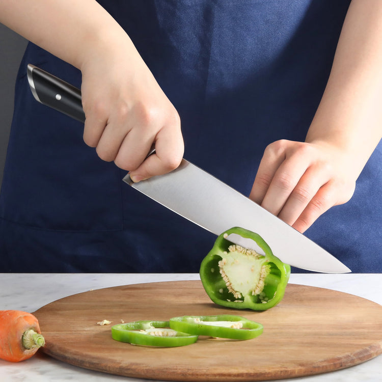 Hands slicing a green bell pepper on a wooden cutting board with a large kitchen knife.