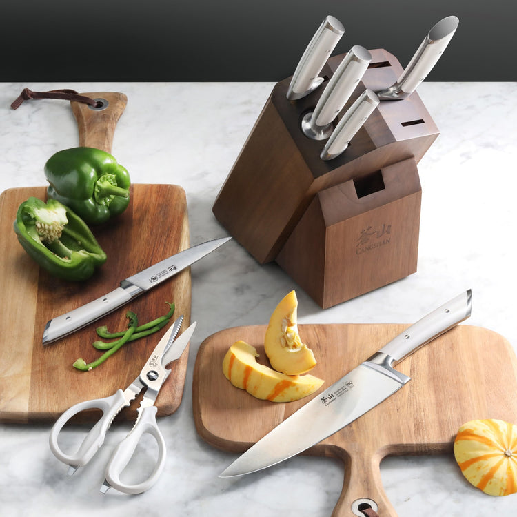 Knife block set with six knives, kitchen shears, and cutting boards holding sliced green pepper and pumpkin pieces.