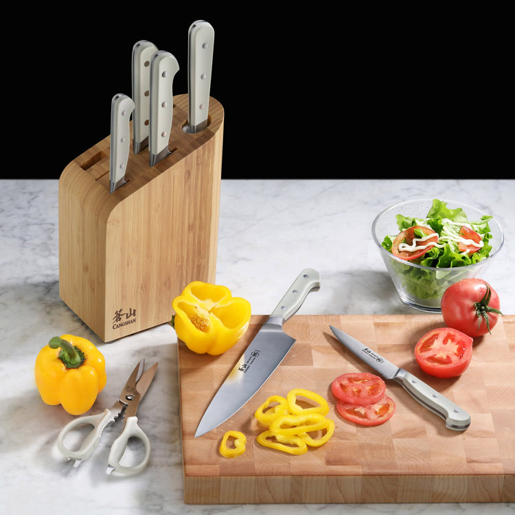 Bamboo knife block with five stainless steel knives, cutting board with sliced tomatoes and yellow bell pepper, salad bowl, a